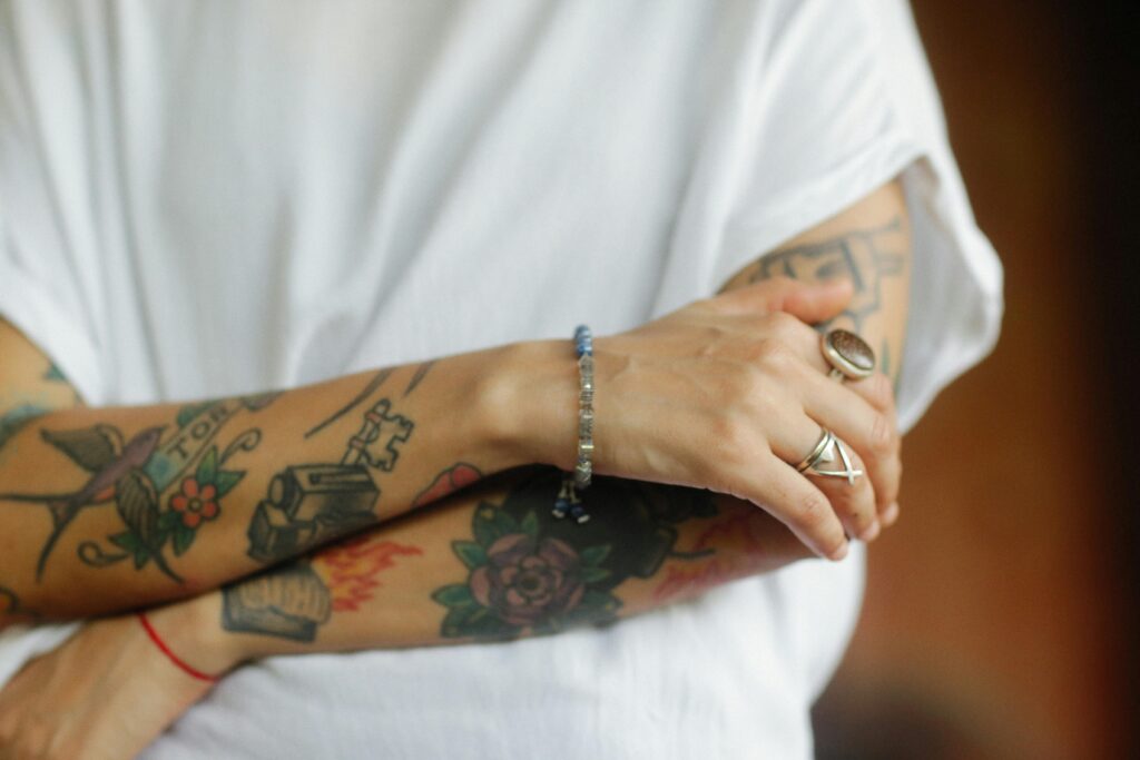 Valkoiseen t-paitaan pukeutunut henkilö pitelee tatuoituja käsivarsiaan vartalonsa edessä. Kuvassa näkyy ainoastaan keskivartalo.
