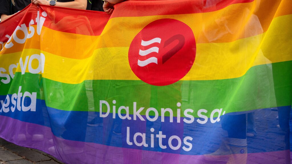 Lähikuva sateenkaaren värisestä banderollista, jossa Diakonissalaitoksen logo.